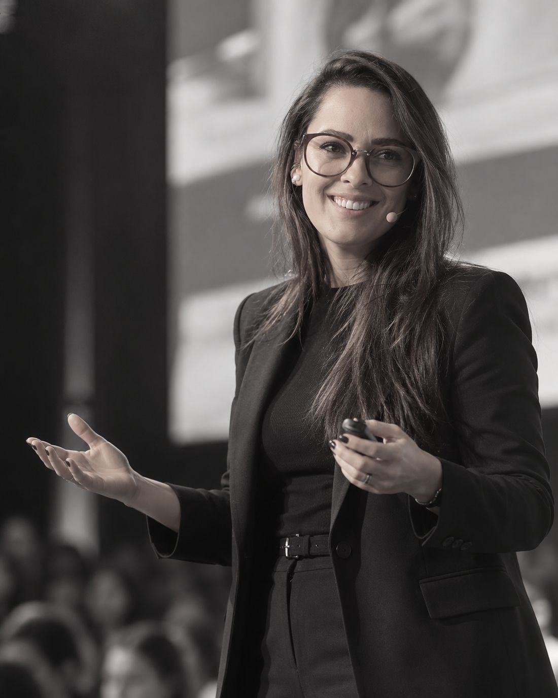 Grazi Guaspari sorrindo durante uma palestra, com a plateia ao fundo